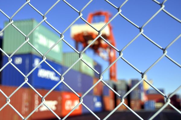 Shipping containers behind a chain-link fence during the day for story about the USMCA