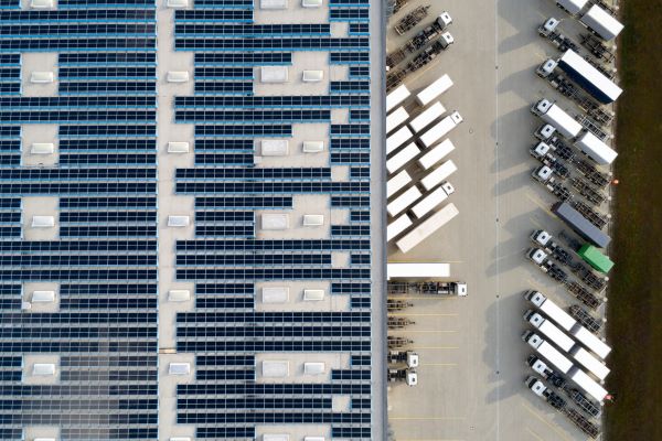 Aerial view of solar panels on a warehouse roof with trucks parked next to it