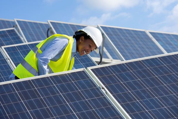 A black woman in a neon construction vest smiles while inspecting solar panels on a sunny day