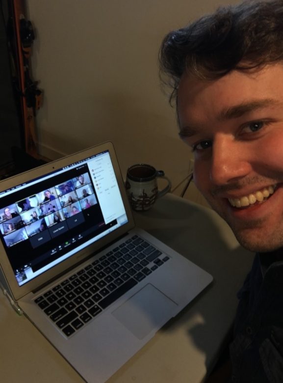 Smiling man sitting next to laptop computer in a virtual meeting with many children