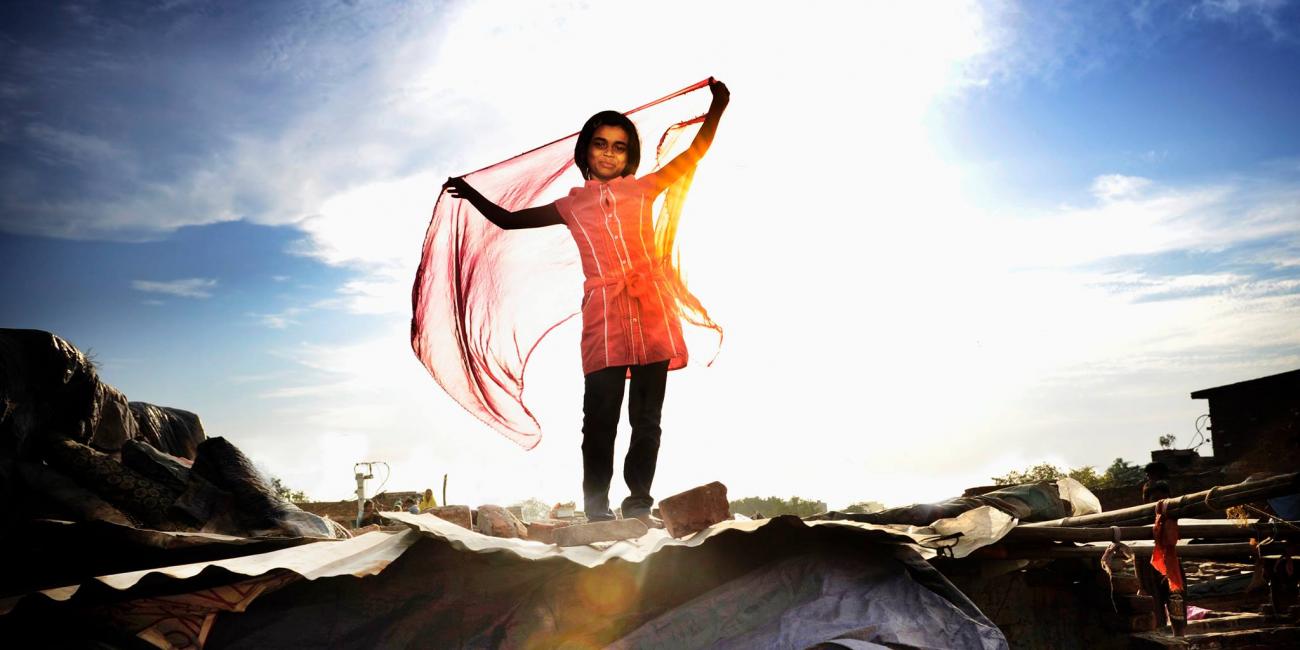 Little girl standing on a shack (in a slum). Sunlight is behind her.
