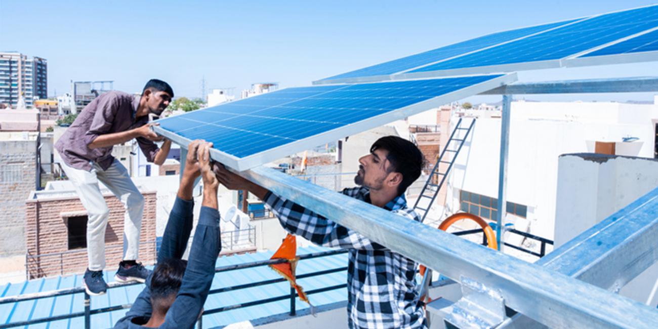 Three workers install solar panels on a roof