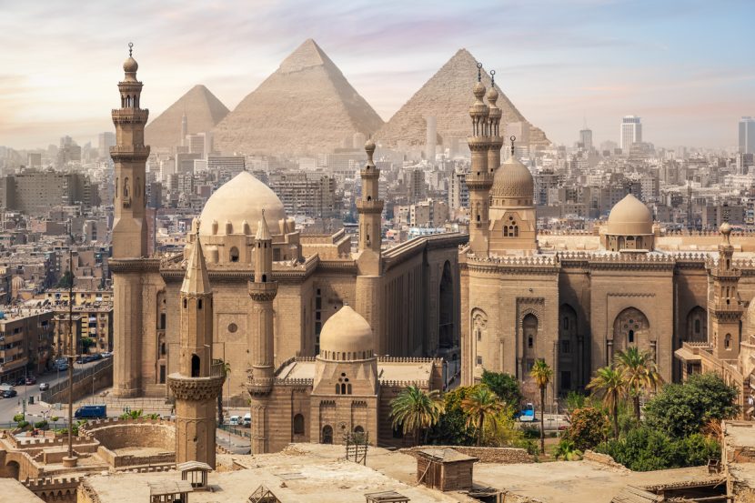 A mosque is pictured against the Cairo skyline with three pyramids in the background.