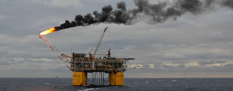 An offshore oil rig appears with a flare and plume of black smoke.