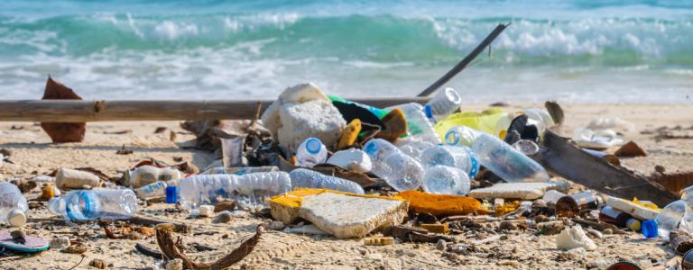 A pile of plastic rubbish on a beach. In the background, waves from the sea wash up on shore.