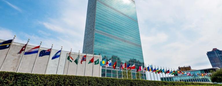 The United Nations' building in New York, a skyscraper, with countries' flags raised in front of the building