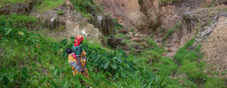 Woman carrying a baby on her back walks in a rural area in Rwanda