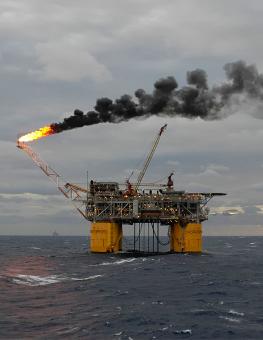 An offshore oil rig appears with a flare and plume of black smoke.