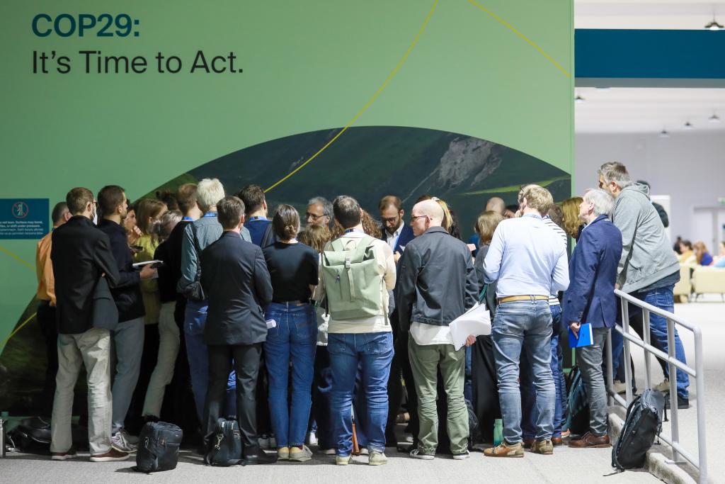 Delegates at COP 29 huddle. In the top right, text reads COP29: It's Time to Act.