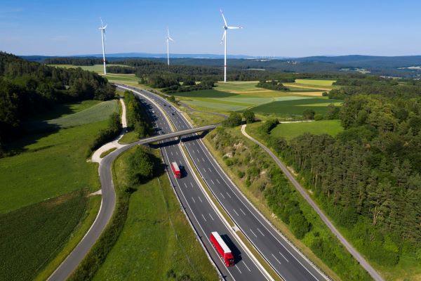 Aerial view of highway in England on a sunny day with green hills and wind turbines