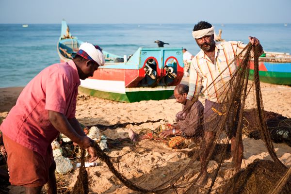 Two fishermen in India lift a fishing net on a sunny day on the beach